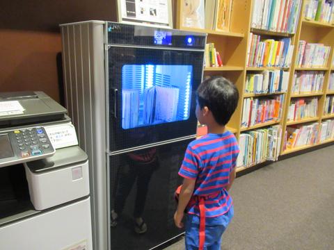 男の子が図書除菌機が本を除菌している様子を眺めている写真
